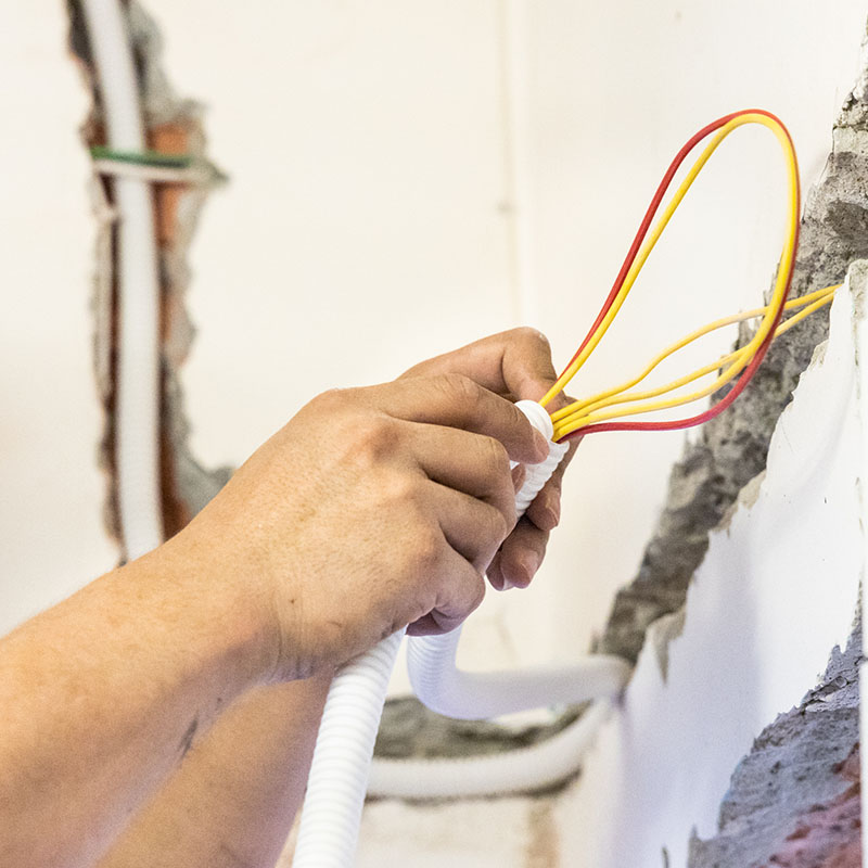 Electrician concealing electicity power wire lines within plastic tube embed into wall